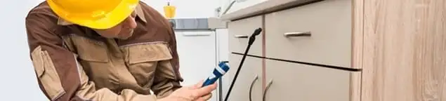 Roach exterminator applying treatment under kitchen cabinets in Tampa, FL