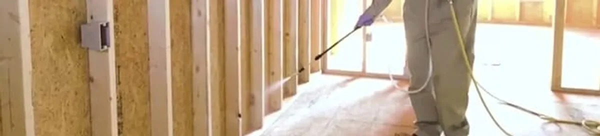 Termite treatment technician applying spray along framing and unfinished walls in Tampa, FL